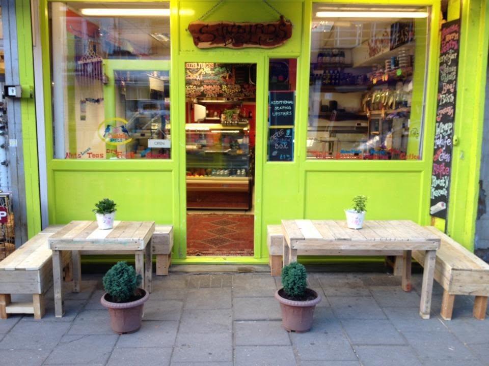 Sunbirds Deli's lime-green frontage, wooden sign, full open entrance and street tables